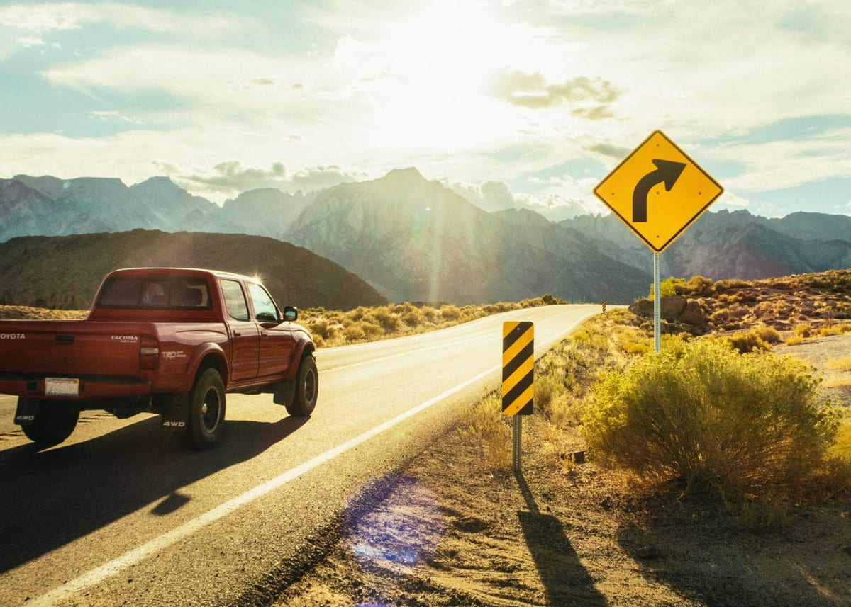 Pickup truck driving a sunlit Texas Hill Country highway past dry brush and hills